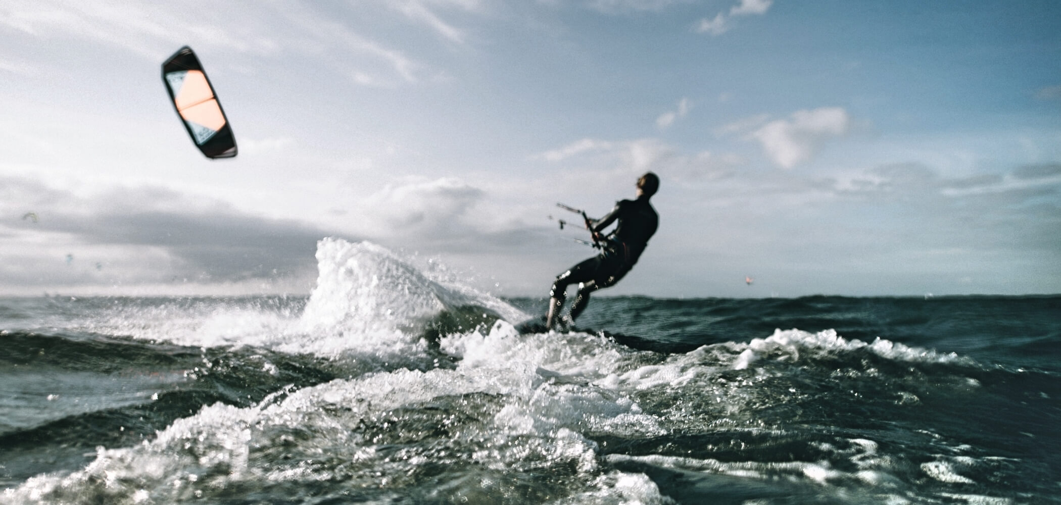 High-adrenaline kitesurfing in untamed waters Kitesurfer riding a powerful wave in open water, surrounded by dynamic winds and spray.